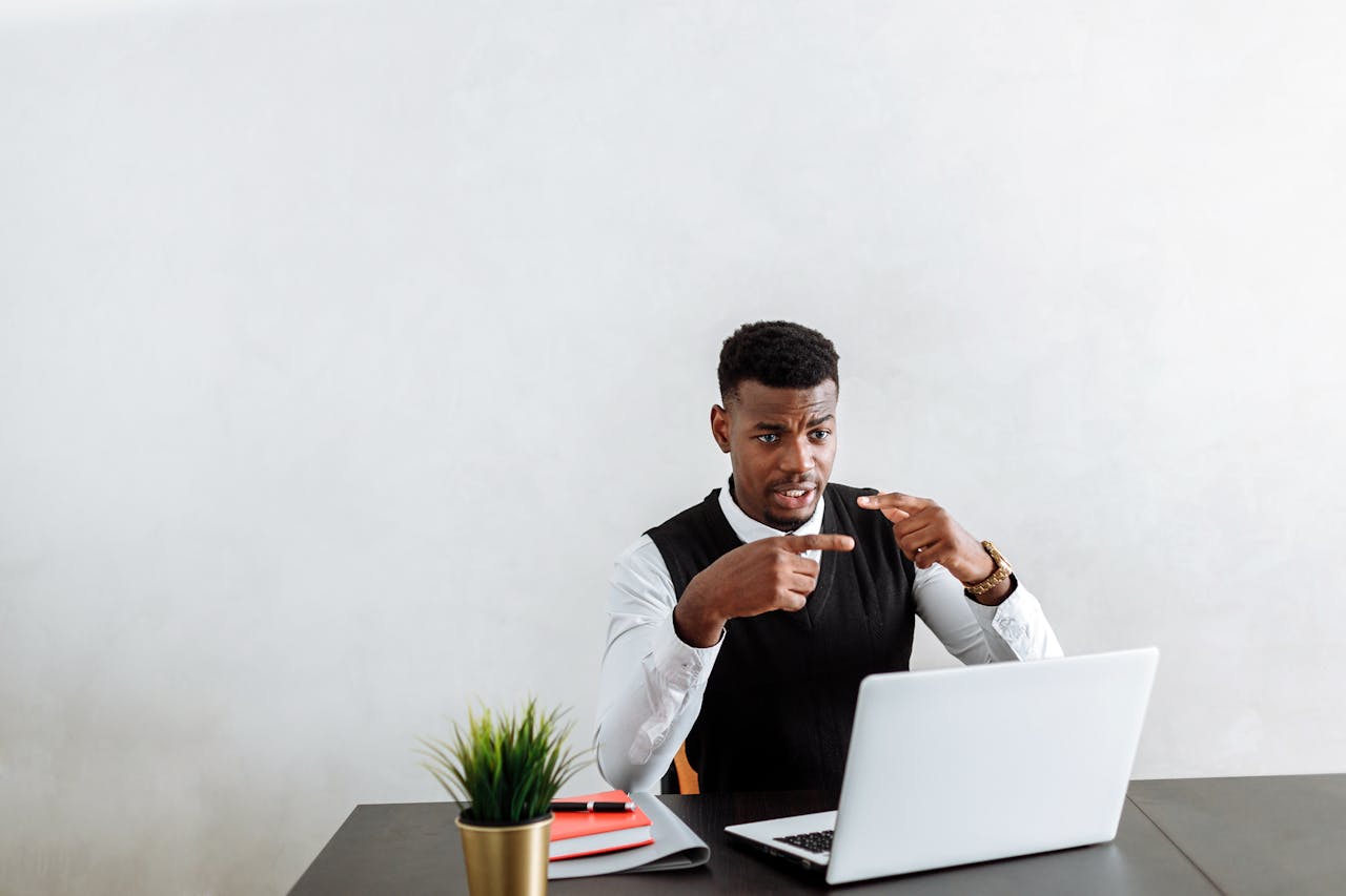 Professional businessman explaining during video call using laptop in modern office setting.